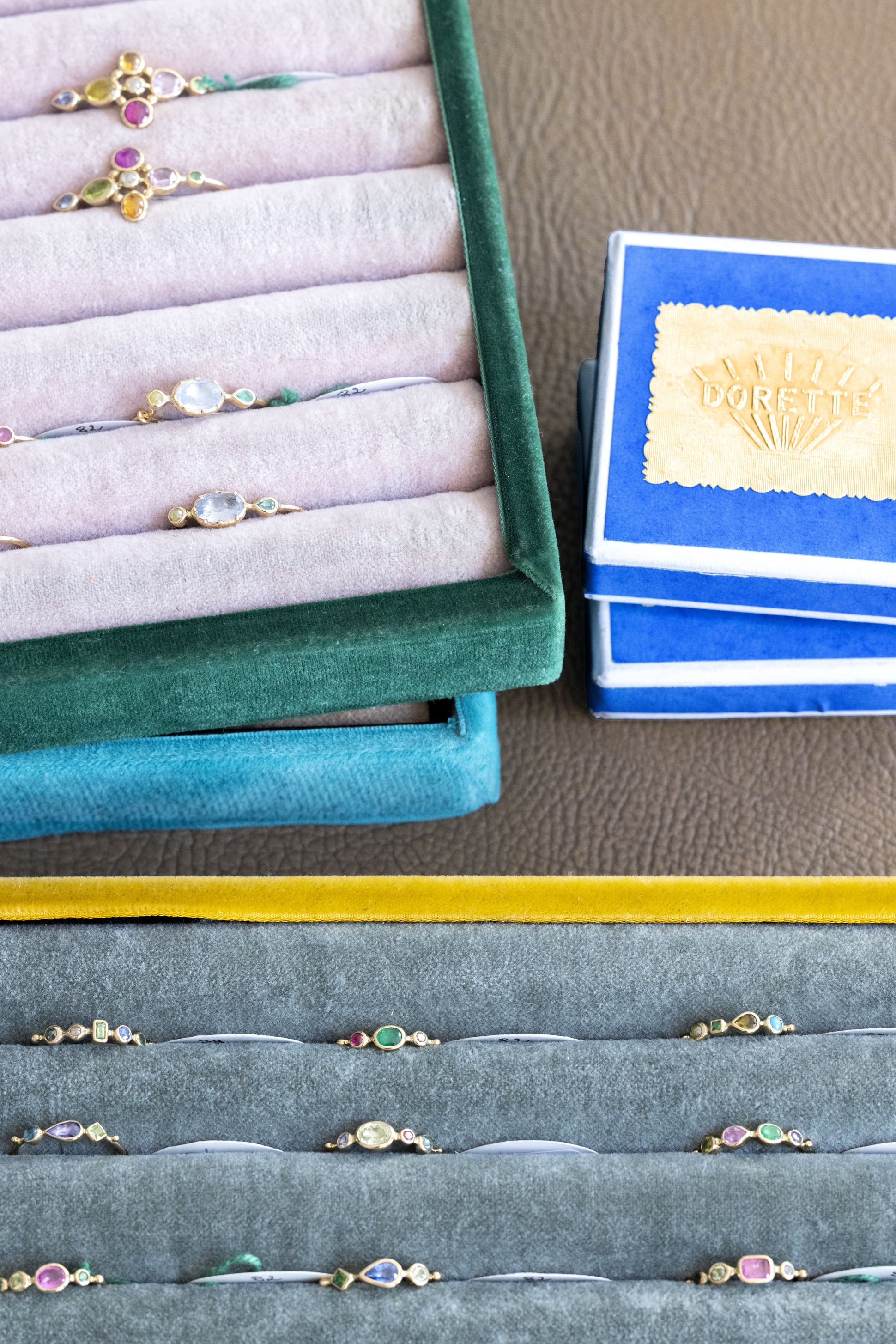 Close-up of colourful Dorette rings set with mixed gemstones, arranged in velvet jewellery trays alongside blue Dorette boxes.