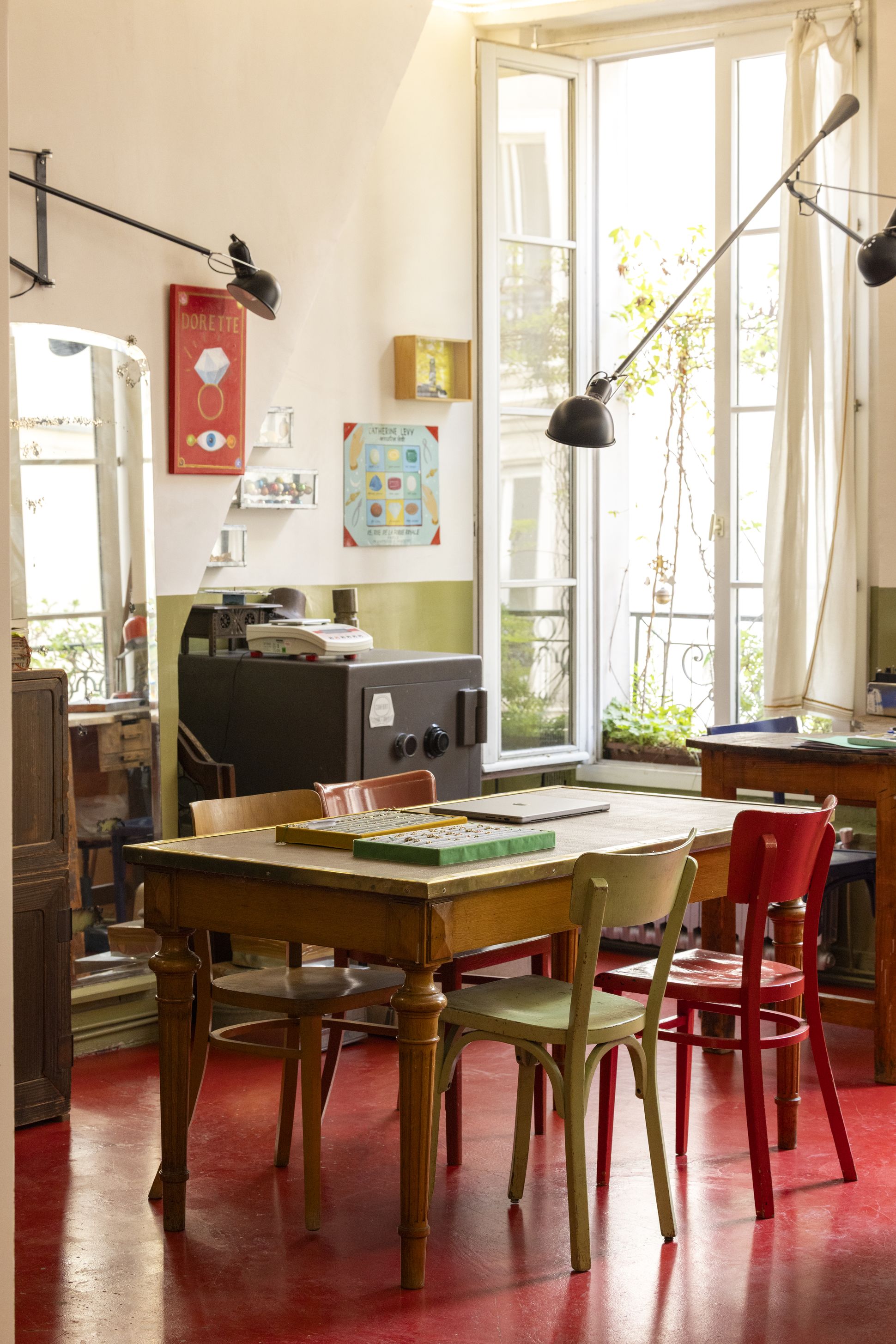 Bright studio space at Dorette, featuring a wooden table with colourful chairs, jewellery trays, large windows, eclectic wall art and industrial lamps.
