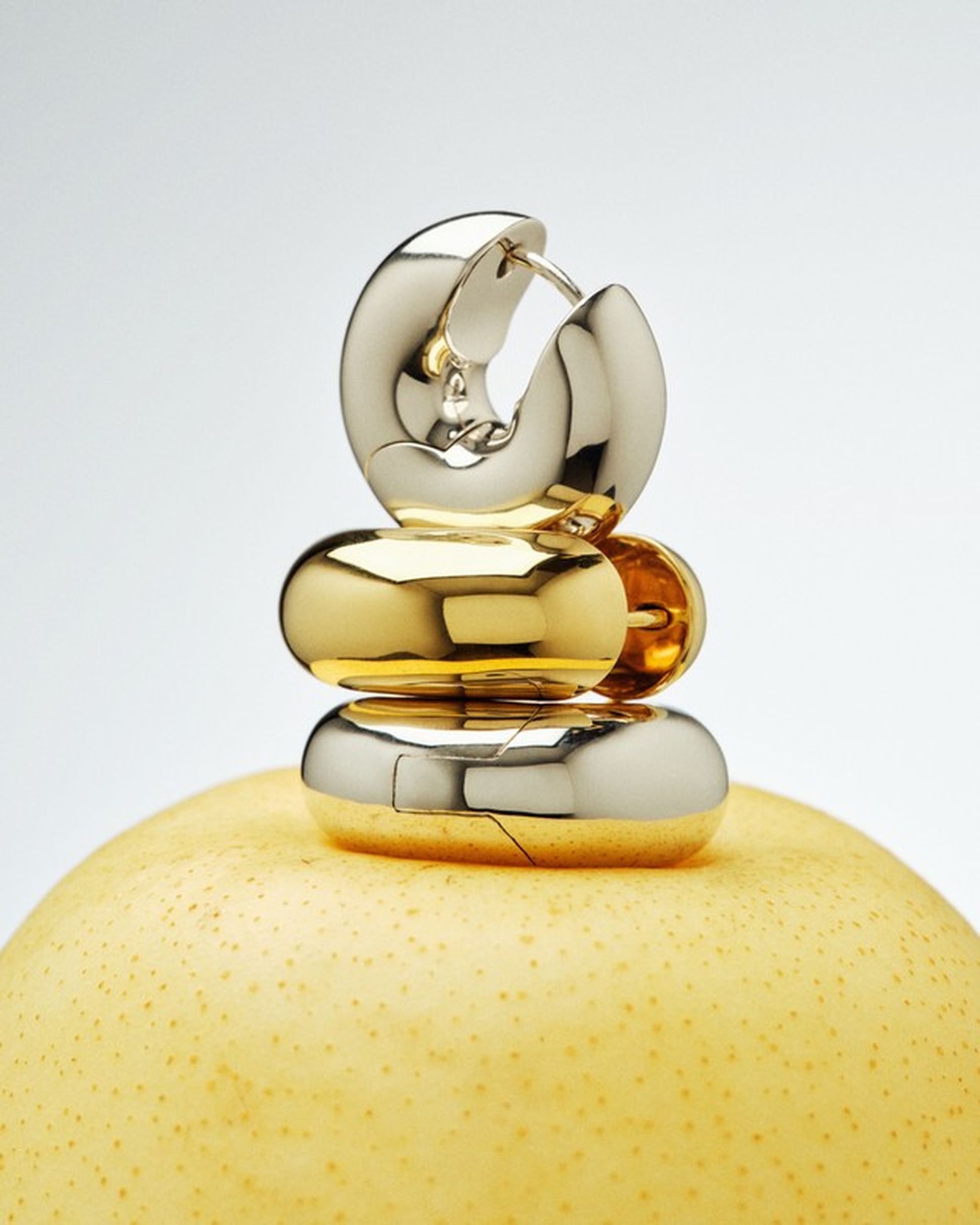 Tom Wood silver and gold earrings with sculptural, minimalist shapes, displayed on a yellow fruit.