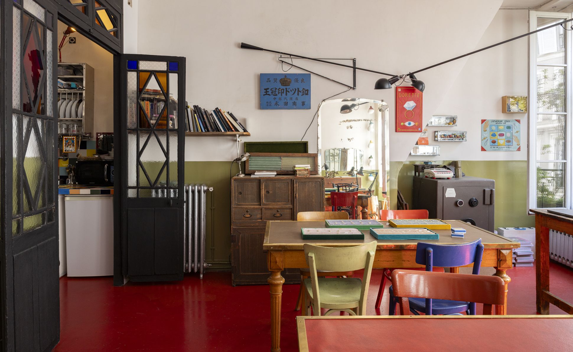 Interior of the Dorette studio, showing a wooden table with colourful chairs, velvet jewellery trays, stained-glass doors, bookshelves, framed artwork and large windows letting in natural light.