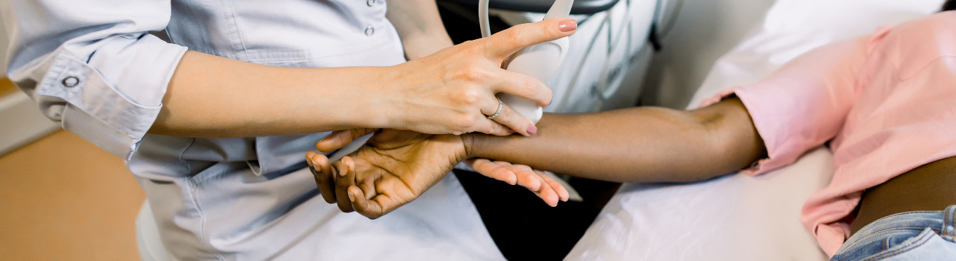 A close up photograph of a sonographer scanning a client's wrist with an ultrasound machine