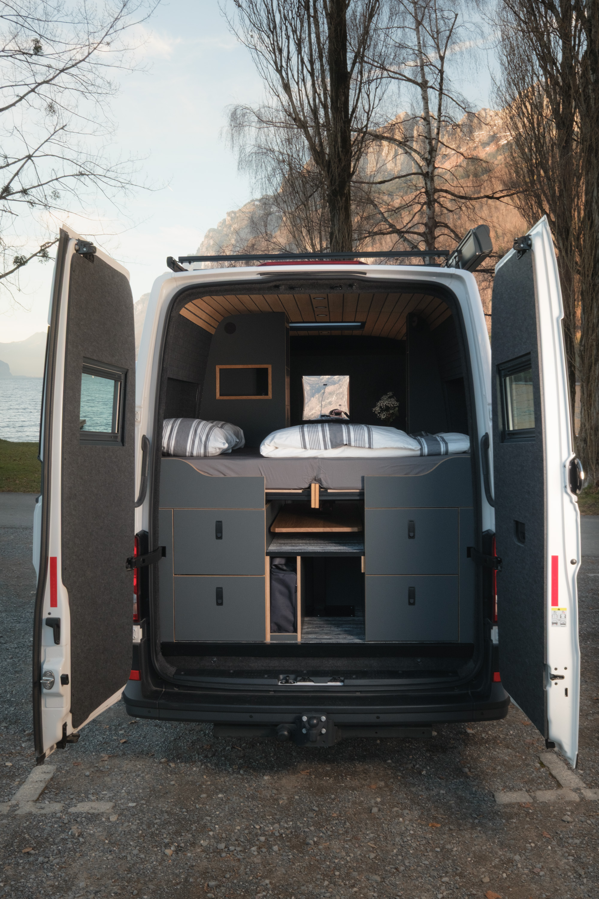 Blick in den hinteren Bereich des Camper Van Ausbaus Patgific von Cocoon Vans. Das Bett ist zusammengefahren. Die Garage besteht auf antrazitschwarzen Fronzen und vier Schubladen