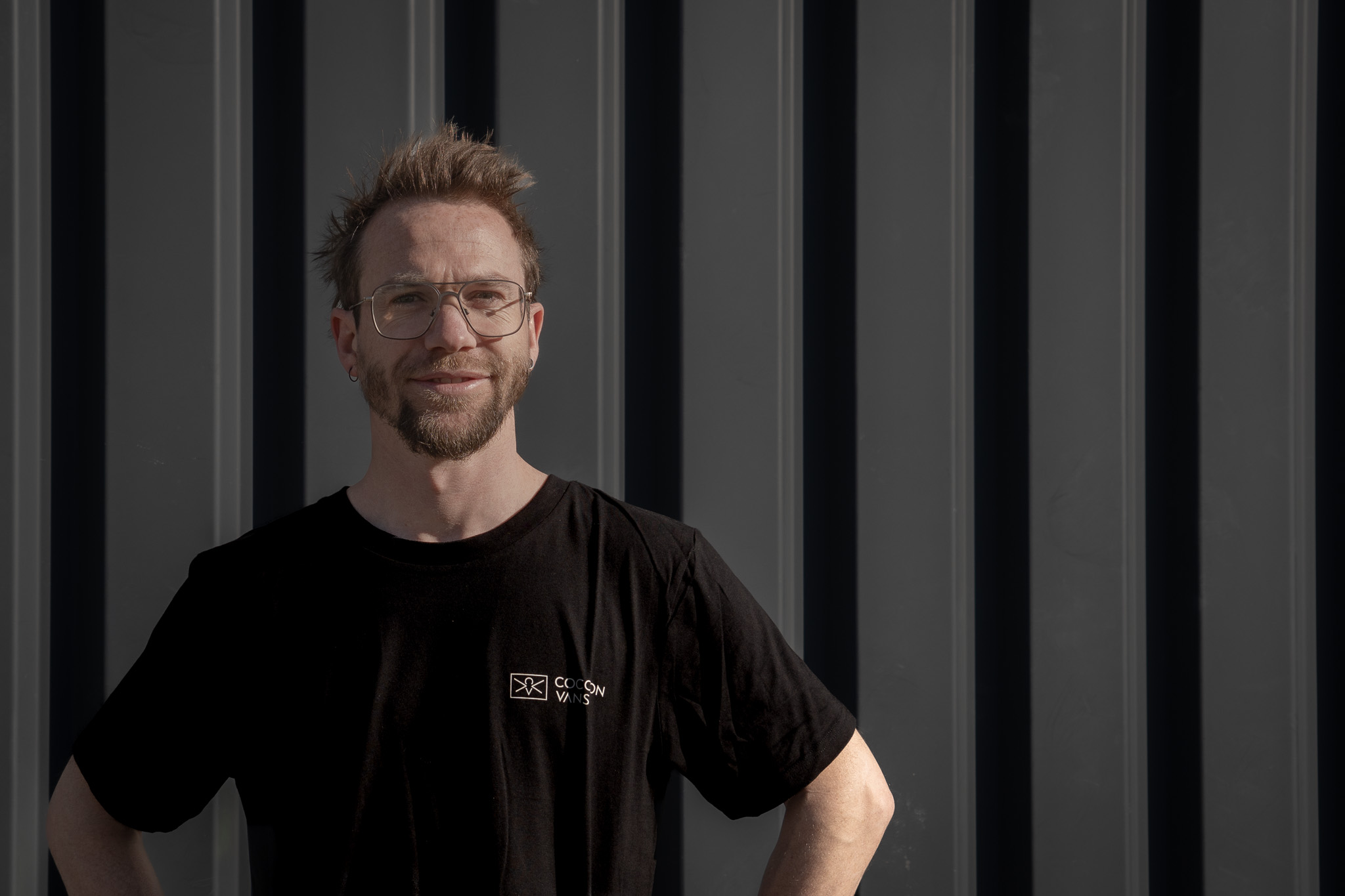 Ferdinand steht vor eine dunklen Wand und blickt gelassen in die Kamera