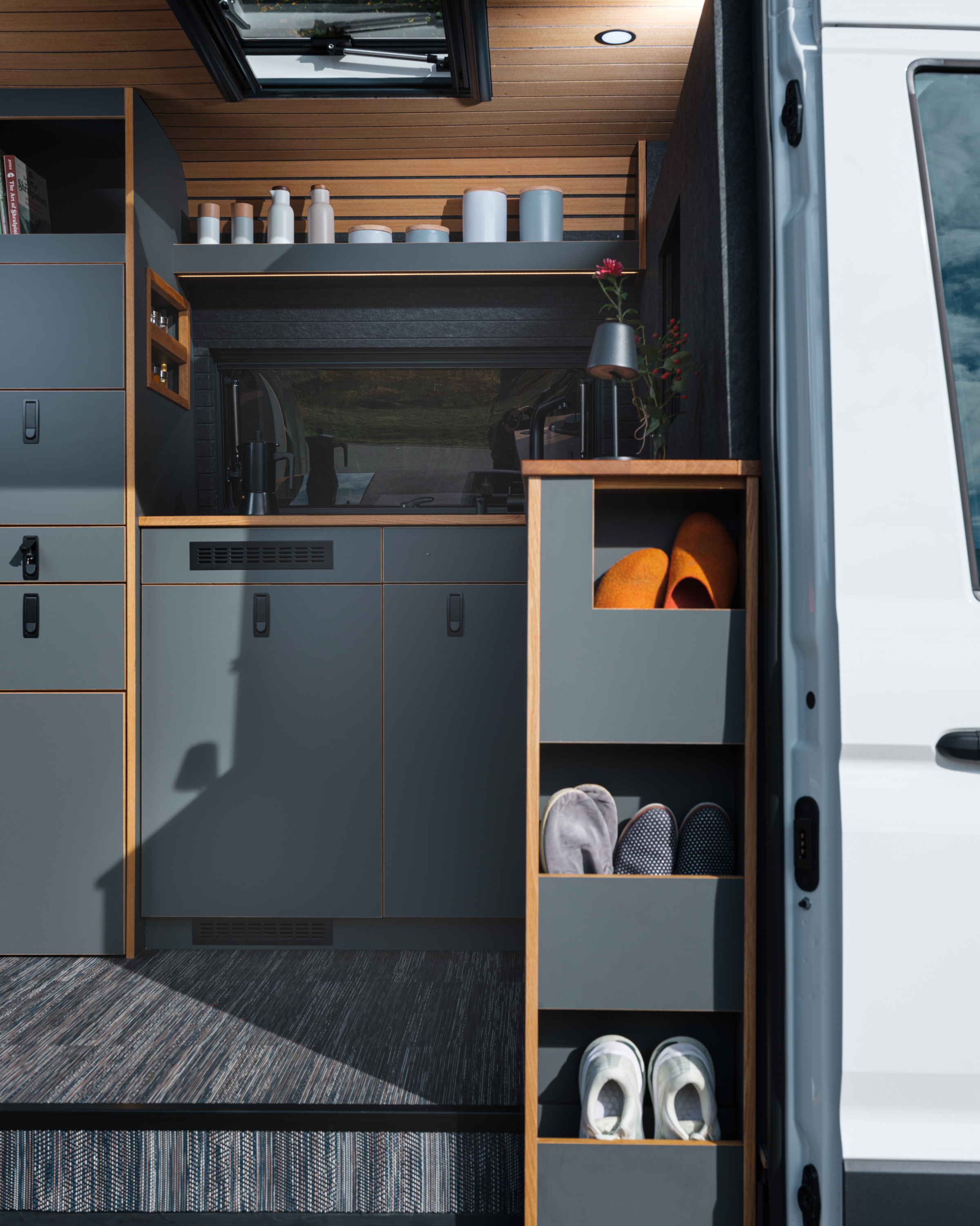 Blick durch die Schiebetüre in den Innenausbau der Kleinserie Patgific von Cocoon Vans. Die fronten sind Antrazitschwarz, die Abschlüsse der Kanten aus Eiche. Auf der Seite des Möbels sieht man sauber verstaute Schuhe