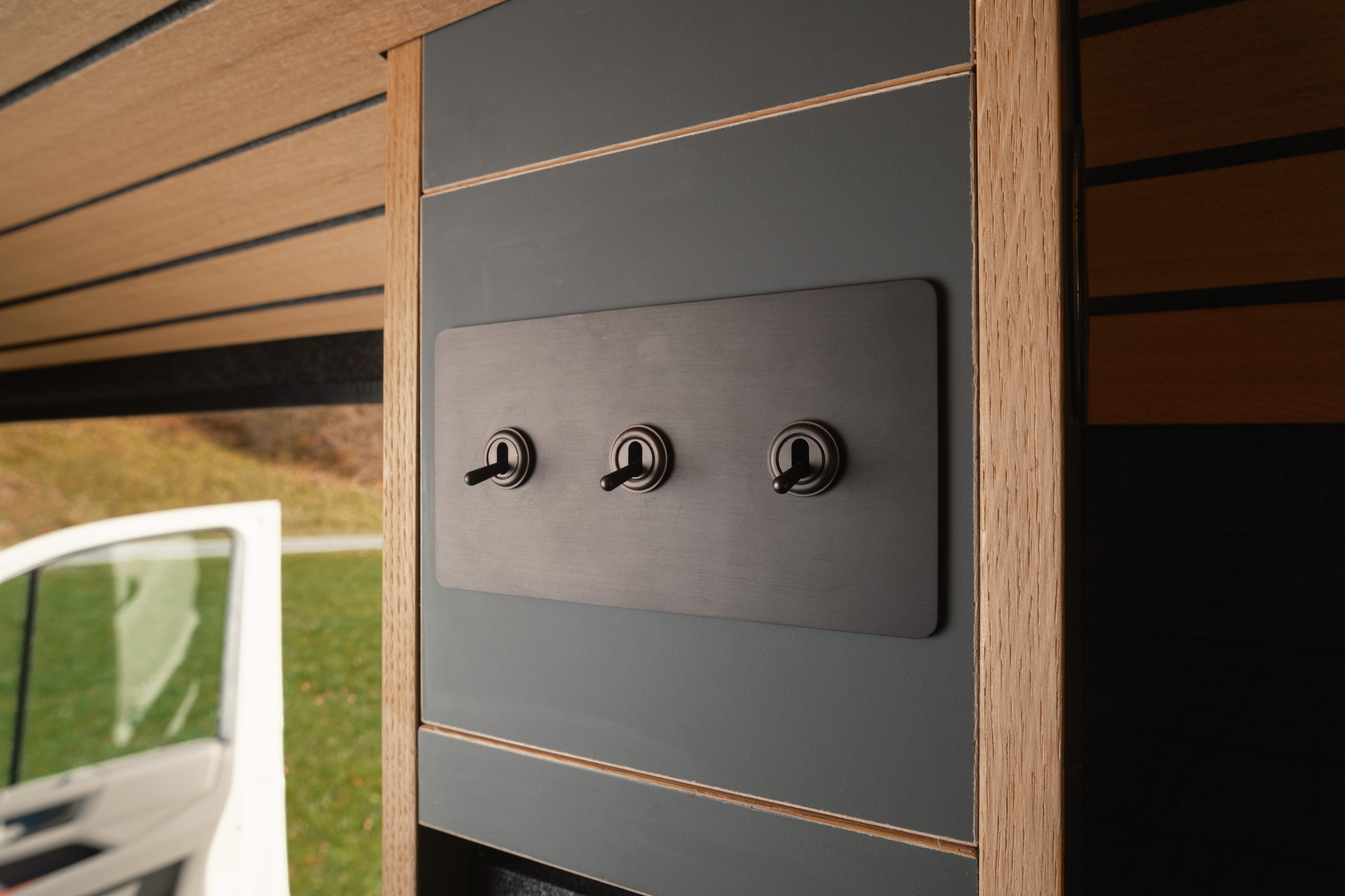 Schwarze Blende auf anthrazitfarbene Möbelbauplatte. 3 Lichtschalter auf Blende wie in einem Flugzeugcockpit. Sehr schlichtes Design und klare Linienführung