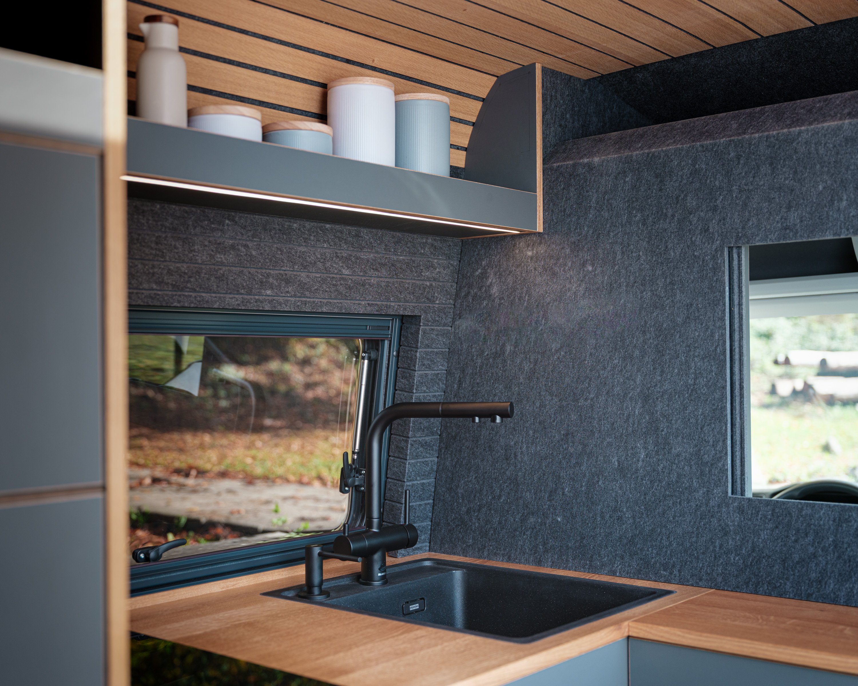 Kleinserie Patgific von Cocoon Vans das schwarze Spülbecken ist in eine edle Ablage aus Eiche eingelassen. die Wände sind aus grauen Filz. Die Decke besteht auch aus Eiche