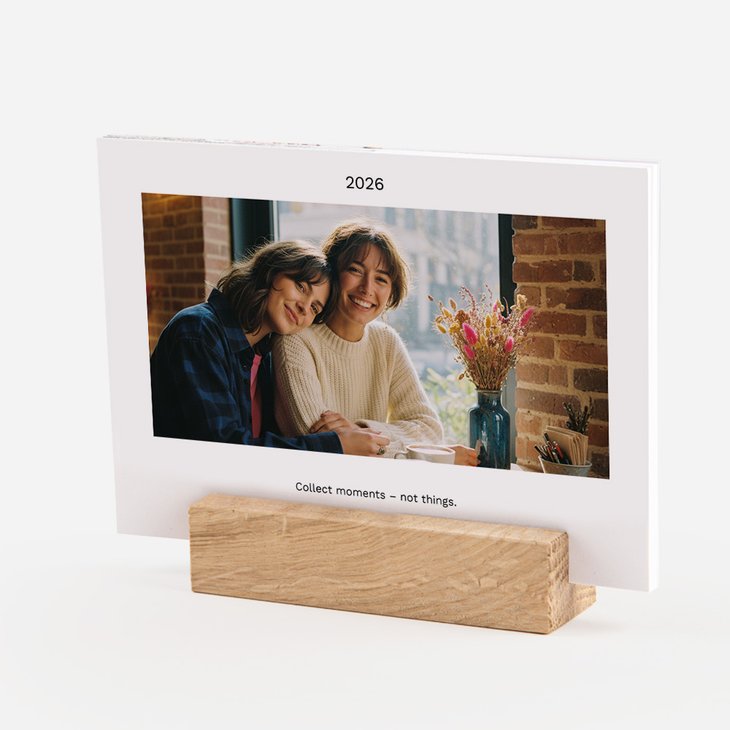 Querformat-Tischkalender auf Eichenholzfuß mit Foto zweier lächelnder Freundinnen an einem Fenster mit Trockenblumen