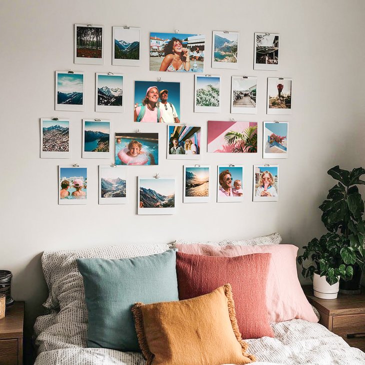 Fotowand mit zahlreichen Fotoabzügen an Metallklammern über einem Bett mit bunten Kissen