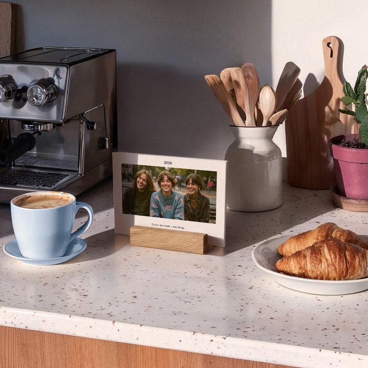 Querformat-Tischkalender mit Foto dreier lachender Freundinnen auf einer Küchenarbeitsplatte neben Kaffee und Croissants