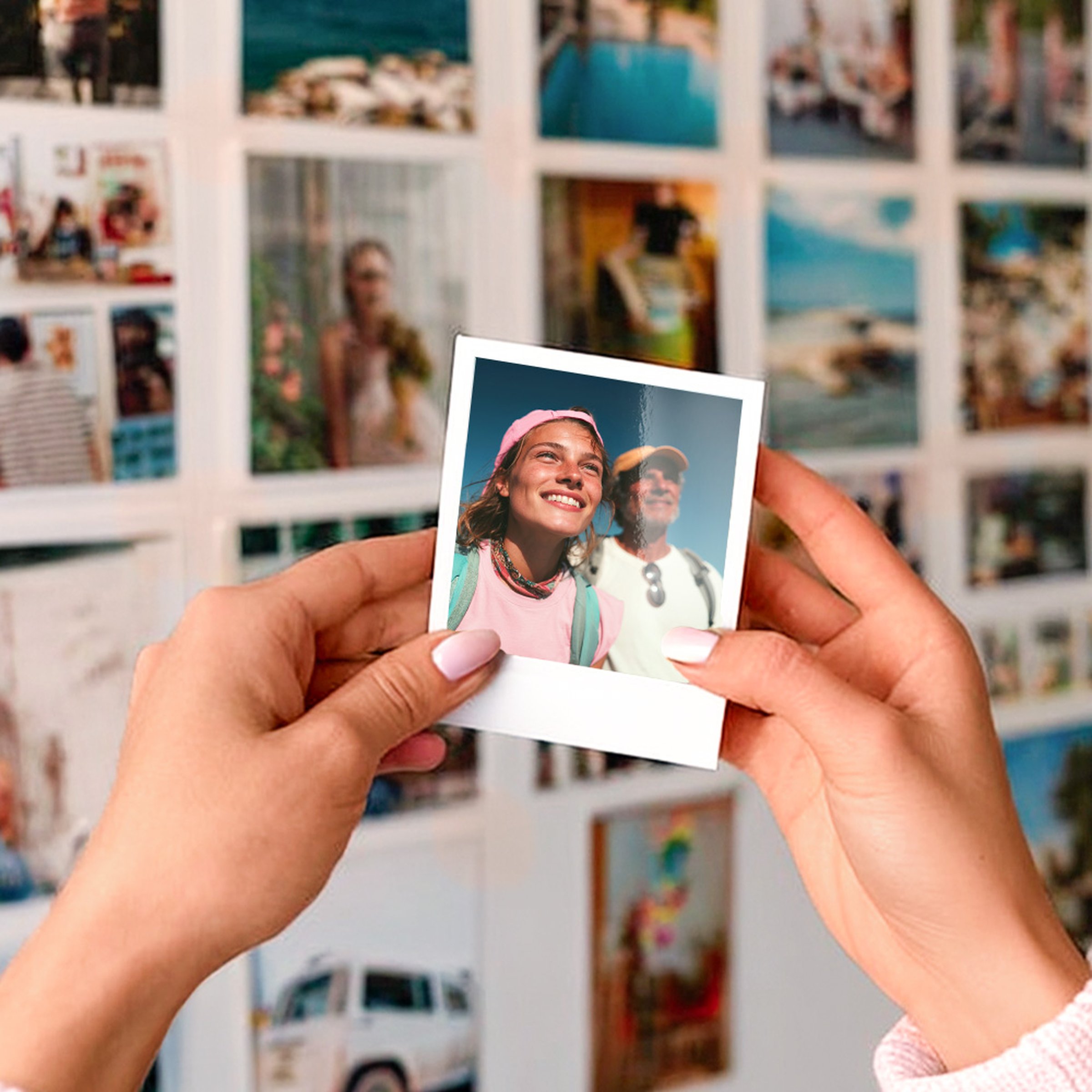 Hände halten einen Retro-Fotoabzug mit Pärchenmotiv vor einer Fotowand mit Urlaubsbildern