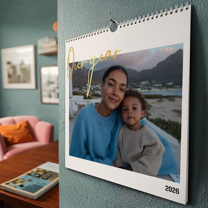 Querformat-Wandkalender mit goldener Schrift „Our year“ und Foto von Mutter mit Kind hängt an einer türkisen Wand