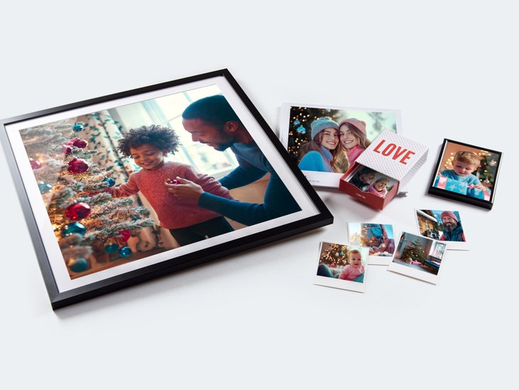 Gerahmtes Foto eines Vaters und seines Kindes beim Schmücken eines Weihnachtsbaums, umgeben von kleineren Familienfotos und einer Bilderbox mit der Aufschrift „Liebe“.
