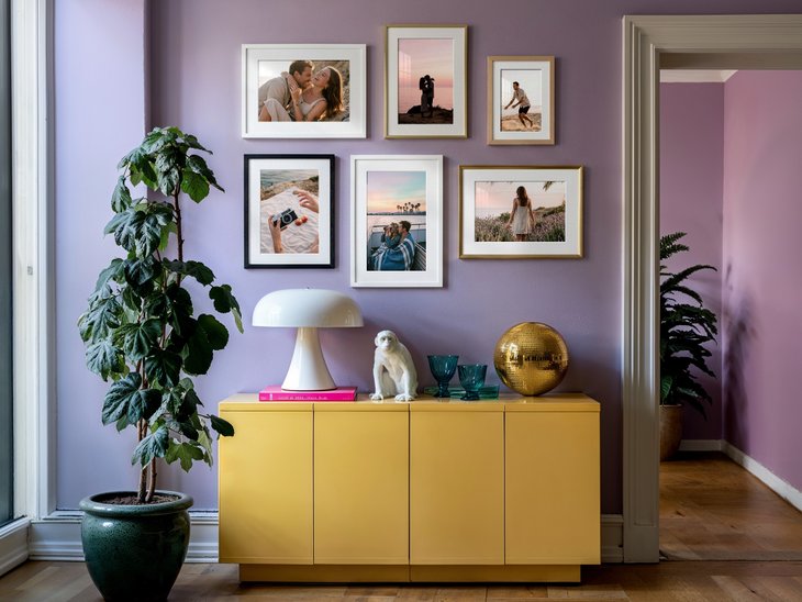 Gallery Wall mit acht gerahmten Fotoabzügen in verschiedenen Formaten an einer fliederfarbenen Wand über einem gelben Sideboard