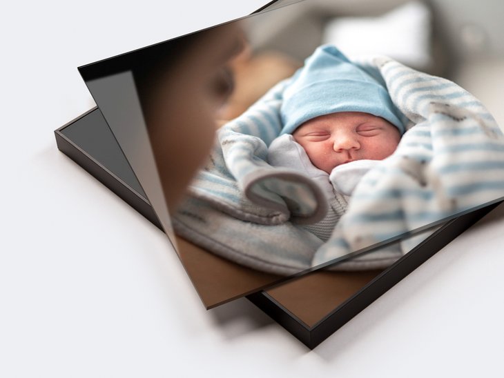 Zwei gestapelte Acrylglasbilder mit Foto eines schlafenden Neugeborenen in blau gestreifter Decke