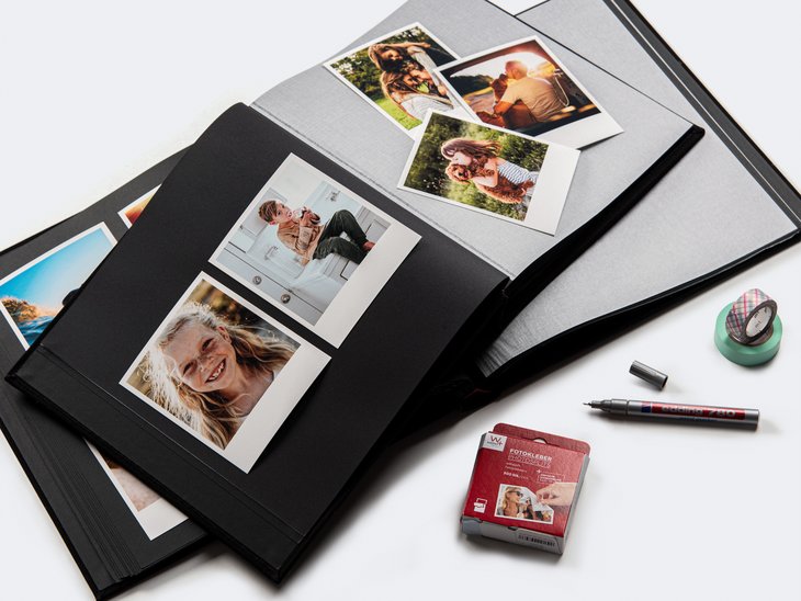 Zwei aufgeschlagene Fotoalben mit eingeklebten Fotoabzügen in verschiedenen Formaten, daneben Fotokleber und Stift