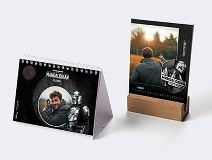 Due calendari da tavolo Star Wars con foto personalizzate sono posizionati uno accanto all’altro. Uno in formato orizzontale con rilegatura a spirale e uno in formato verticale con base in legno.