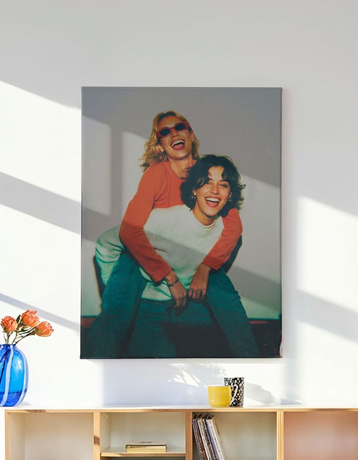 Leinwanddruck im Hochformat mit Freundinnen-Porträt über einem Holzregal mit blauer Vase und Blumen