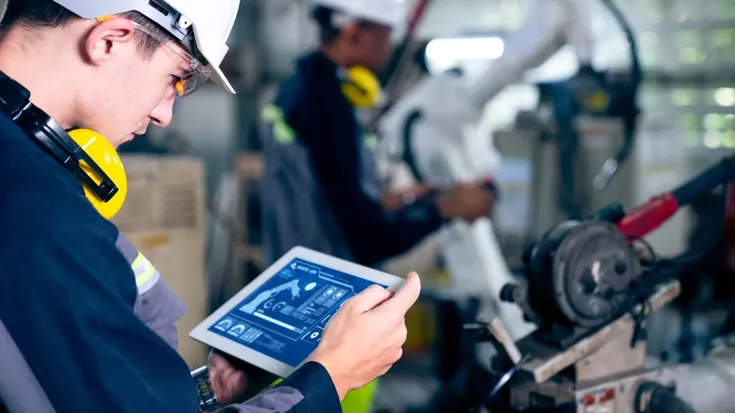 Profissional utilizando tablet em ambiente de automação industrial com máquinas automatizadas