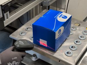 L'opérateur remplit un carton, l’étiquette et le scanne pour transmettre les informations sur sa taille au robot