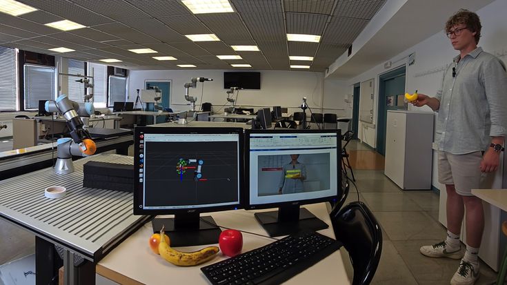 Universal Robots collaborative robot grasps an orange in a robotics lab while AI vision software tracks fruit handling