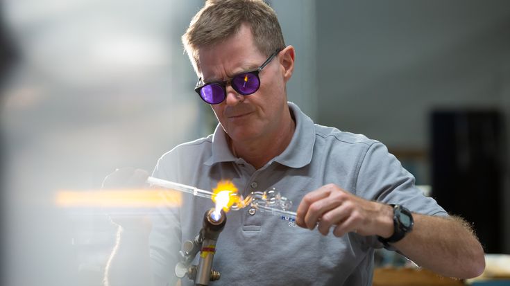 Skilled technician performing precision glasswork with a flame torch, highlighting craftsmanship and innovation supported by the UR+ ecosystem and certified partner solutions.