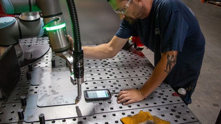 Technician wearing safety glasses adjusts a Universal Robots collaborative robot for a welding application at a metal workbench.
