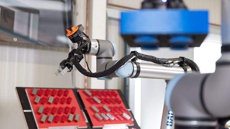 Universal Robots collaborative robot arm equipped with a gripper end effector, handling parts in an industrial workstation.