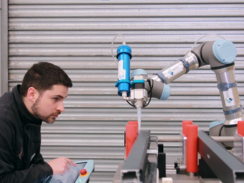 Sobre a mesa, o montador configura o cobot e coloca os quatro perfis na cunha
