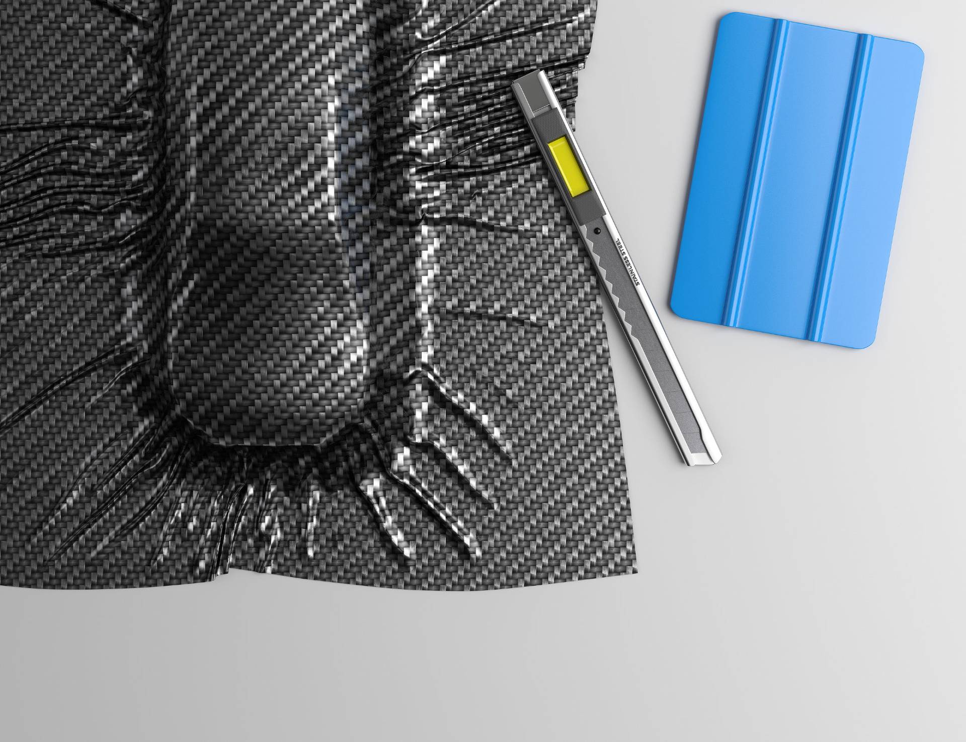Carbon fiber plate with utility knife and blue squeegee on a white background.
