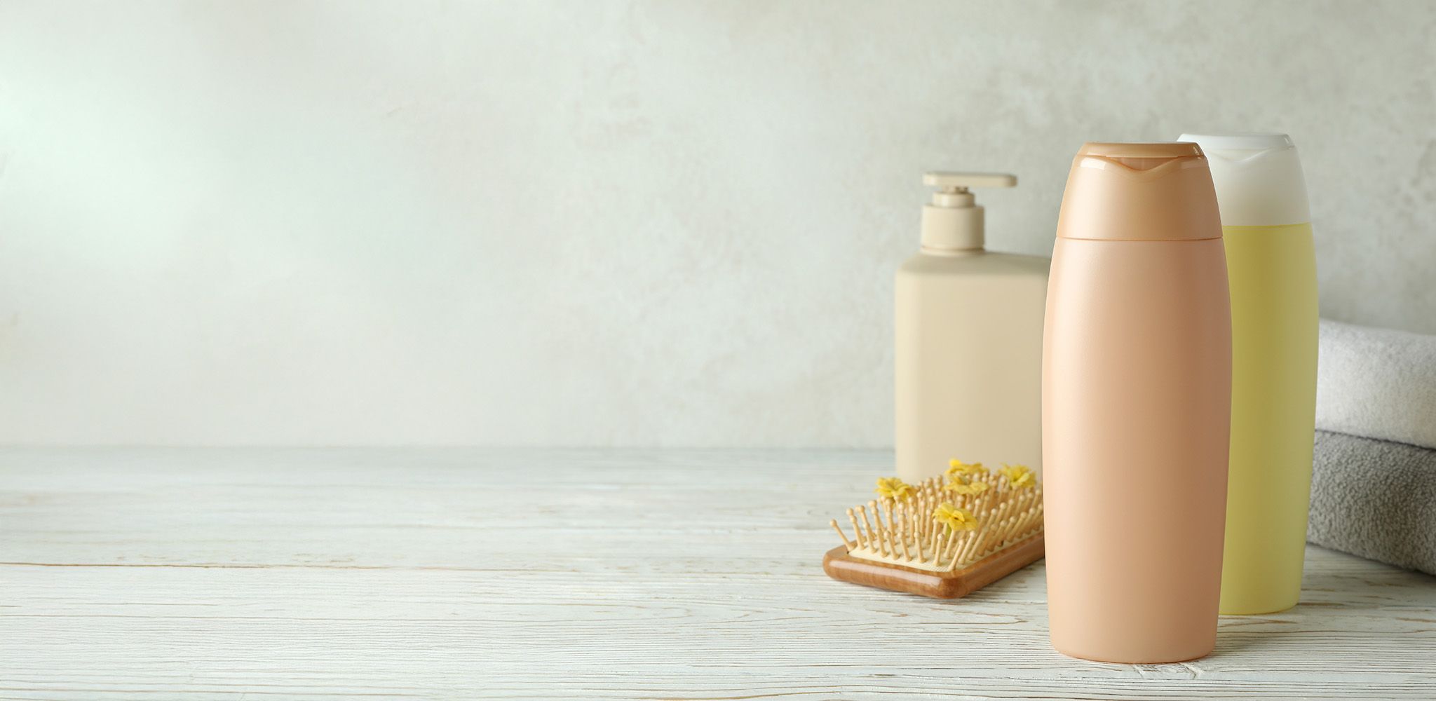 Verschiedene Pflegeprodukte auf einem Holztisch, einschließlich einer Shampooflasche und einem Flüssigseifenspender, neben einer Haarbürste.