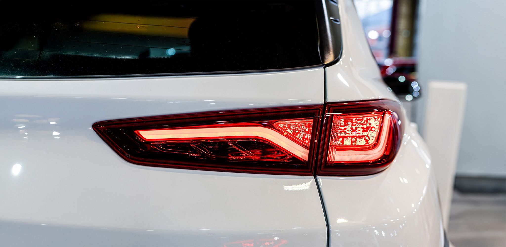 Nahaufnahme des Heckbereichs eines weißen Autos mit rot leuchtenden Rücklichtern, das sich durch modernes Design und scharfe Kanten auszeichnet.