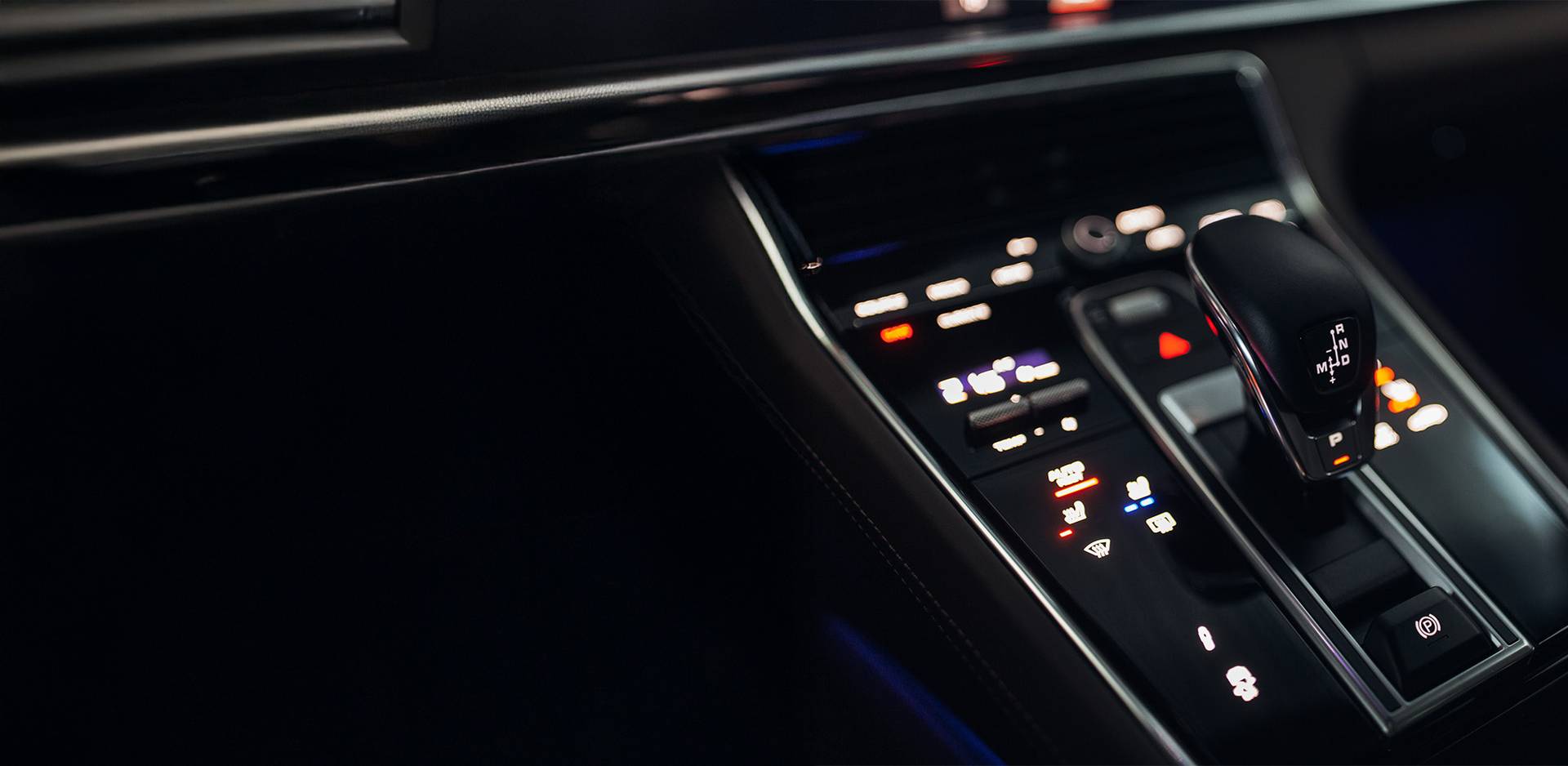Details of the centre console of a luxury car with a modern electronic gear knob and illuminated control panel.