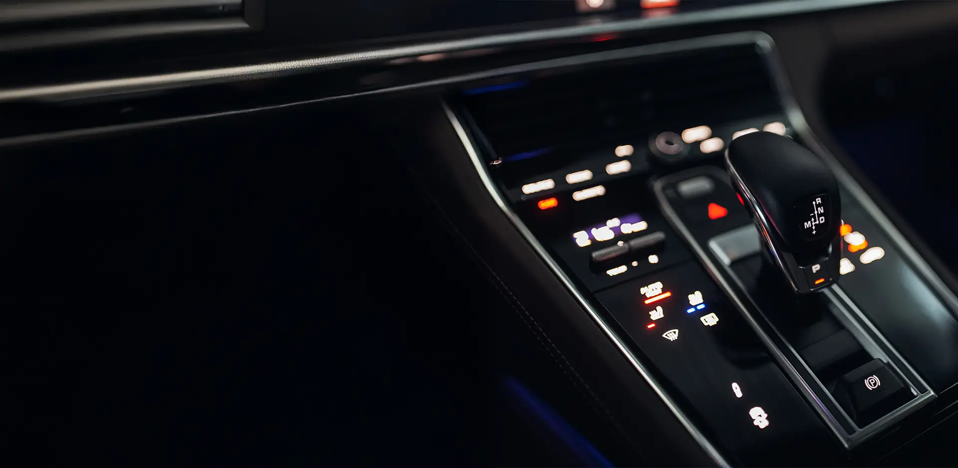 Details der Mittelkonsole eines Luxuswagens mit modernem elektronischen Schaltknauf und beleuchtetem Bedienfeld.