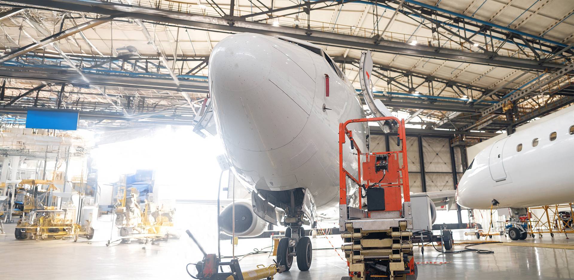 Aircraft in a large maintenance hangar with hydraulic work platform for access to technical components.