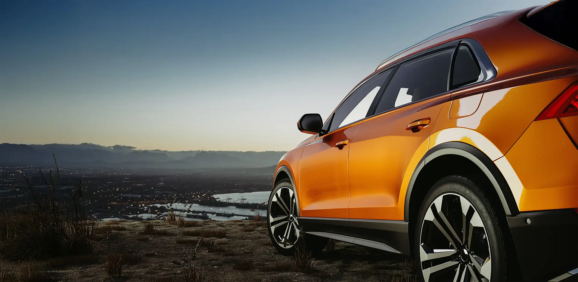 Modern orange SUV on a hill overlooking the cityscape at sunset.