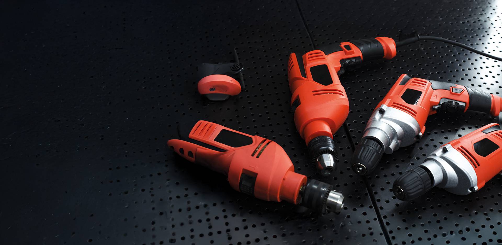 Four red electric drills and a sander on a black, perforated metal table.