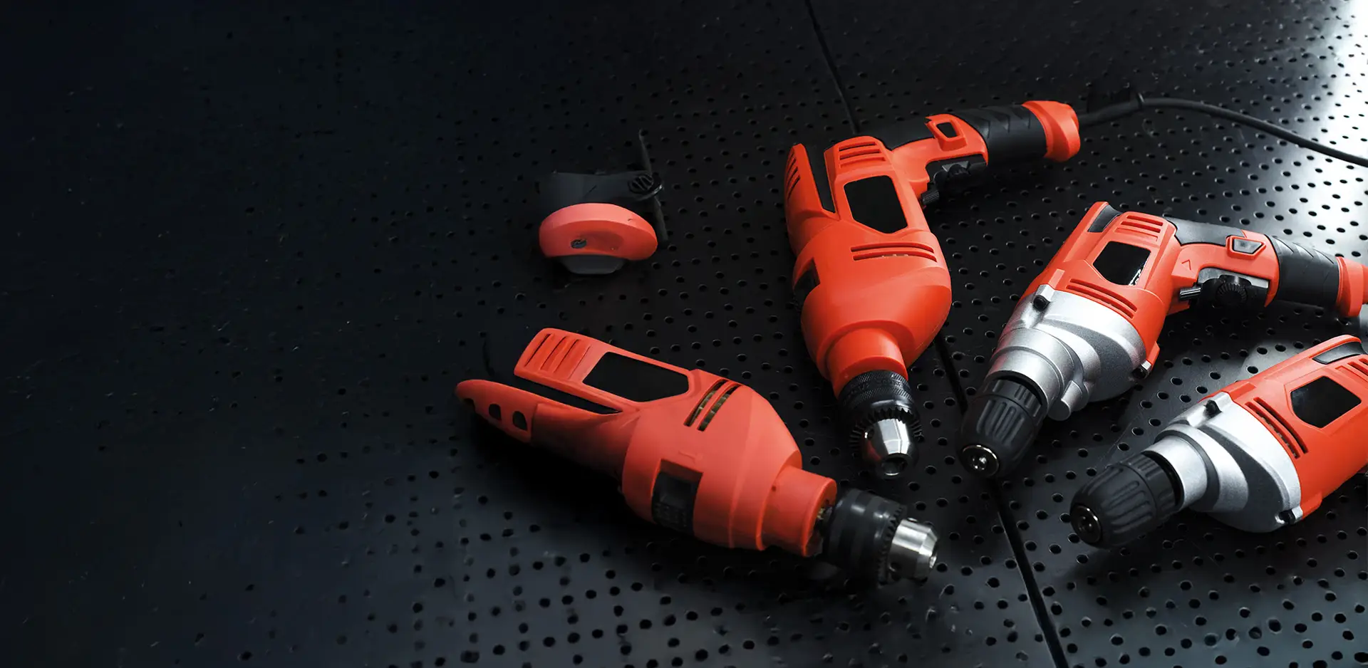 Four red electric drills and a sander on a black, perforated metal table.