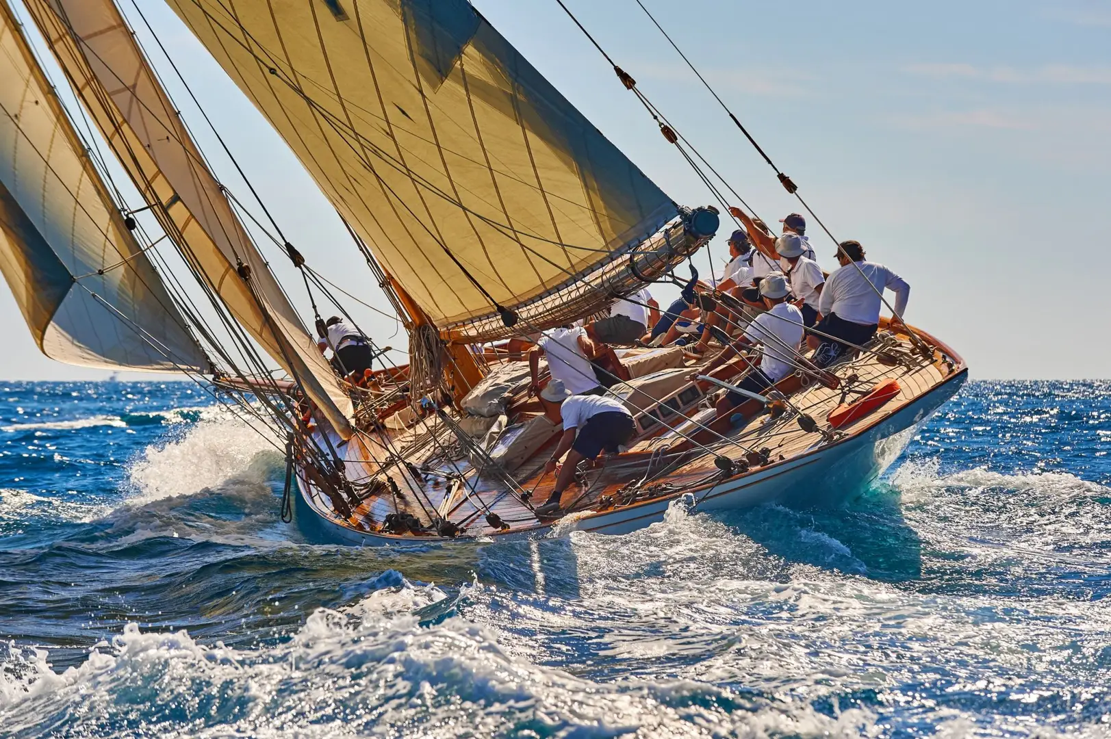 Sailboat with a crew in white shirts navigating through choppy blue waters under clear skies, with sails billowing in the wind.