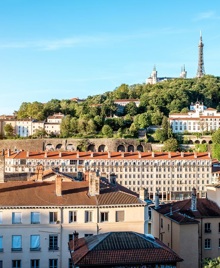 Scenic view over Lyon, France, with historic buildings, lush greenery, and the Basilica of Notre-Dame de Fourvière atop the hill.