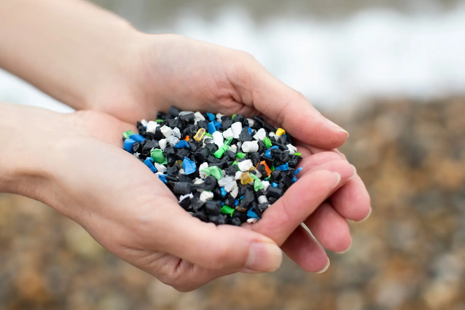 Hands holding small, colorful plastic pellets with a blurred background.
