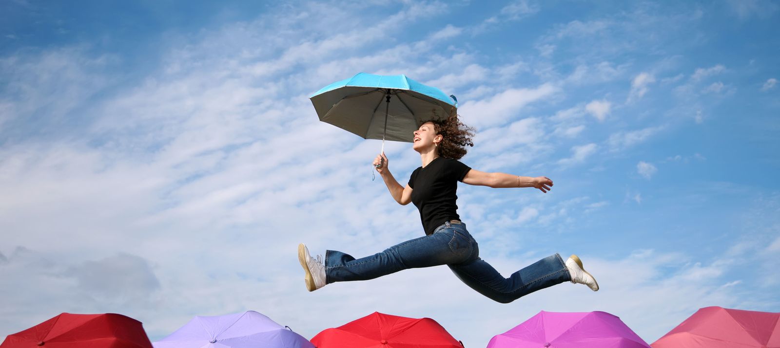 young woman jumps with the umbrella above the umbrellas