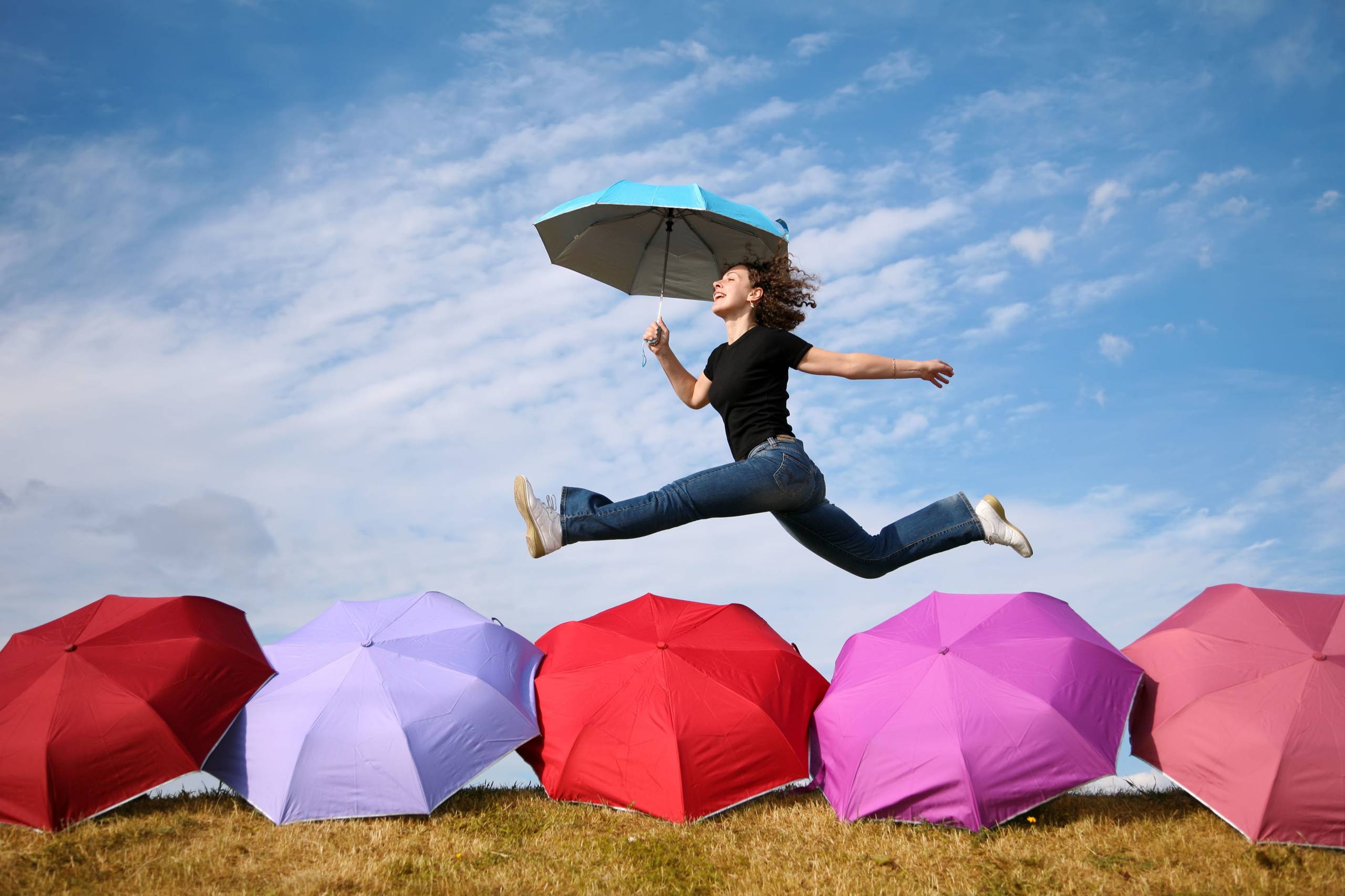 young woman jumps with the umbrella above the umbrellas