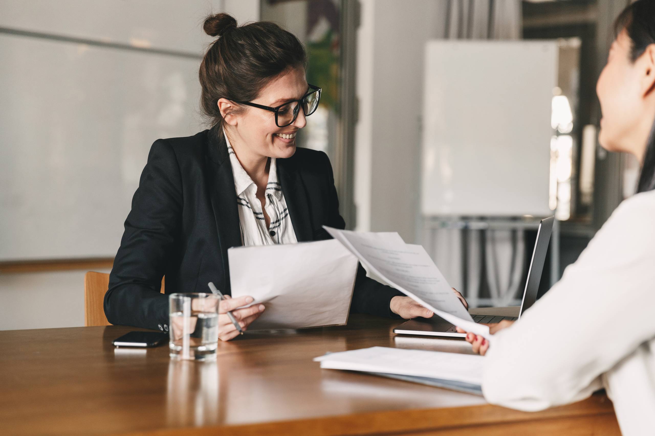 Photo of successful woman holding CV and negotiating with female candidates, during company meeting or job interview