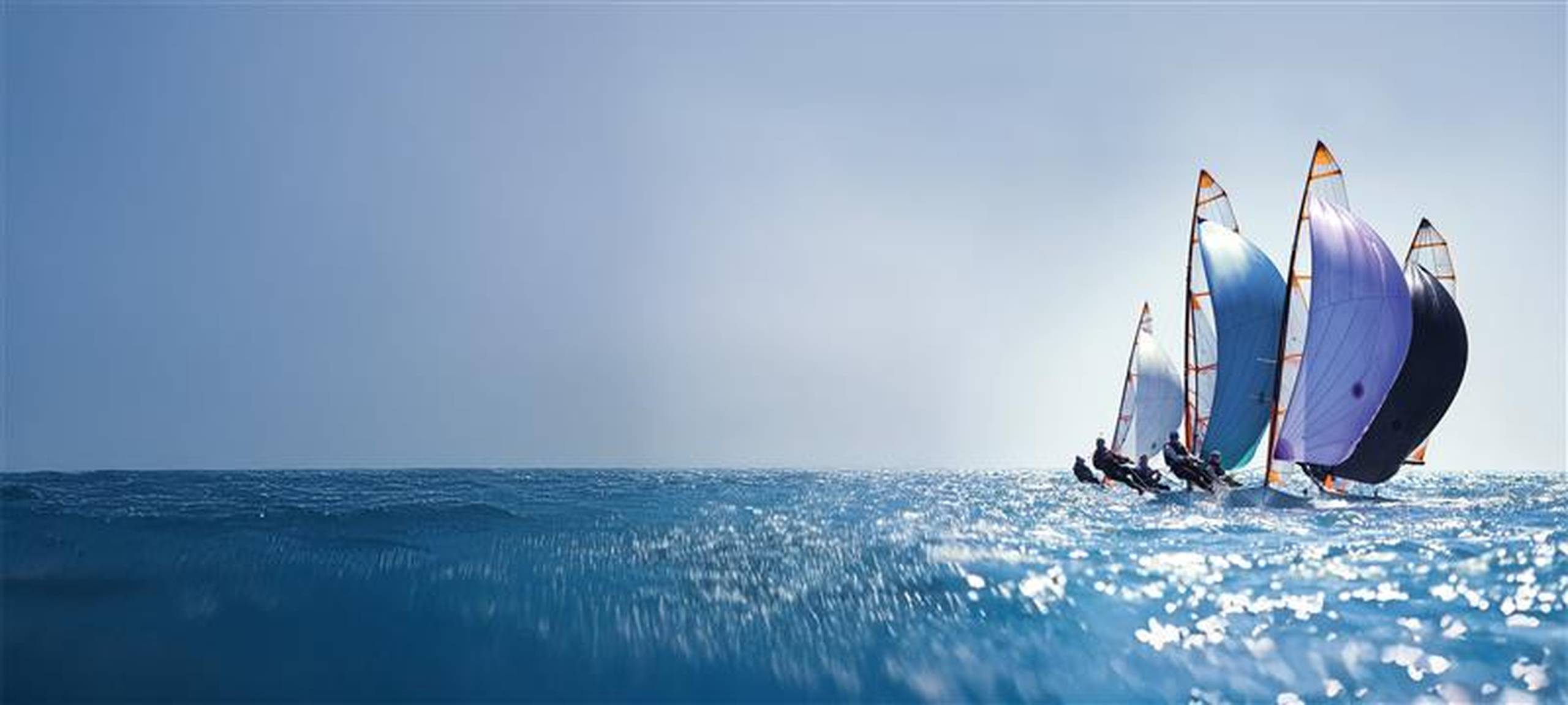 Segelboote mit bunten Segeln liefern sich an einem sonnigen Tag ein Rennen und gleiten unter klarem Himmel über das glitzernd blaue Meerwasser.