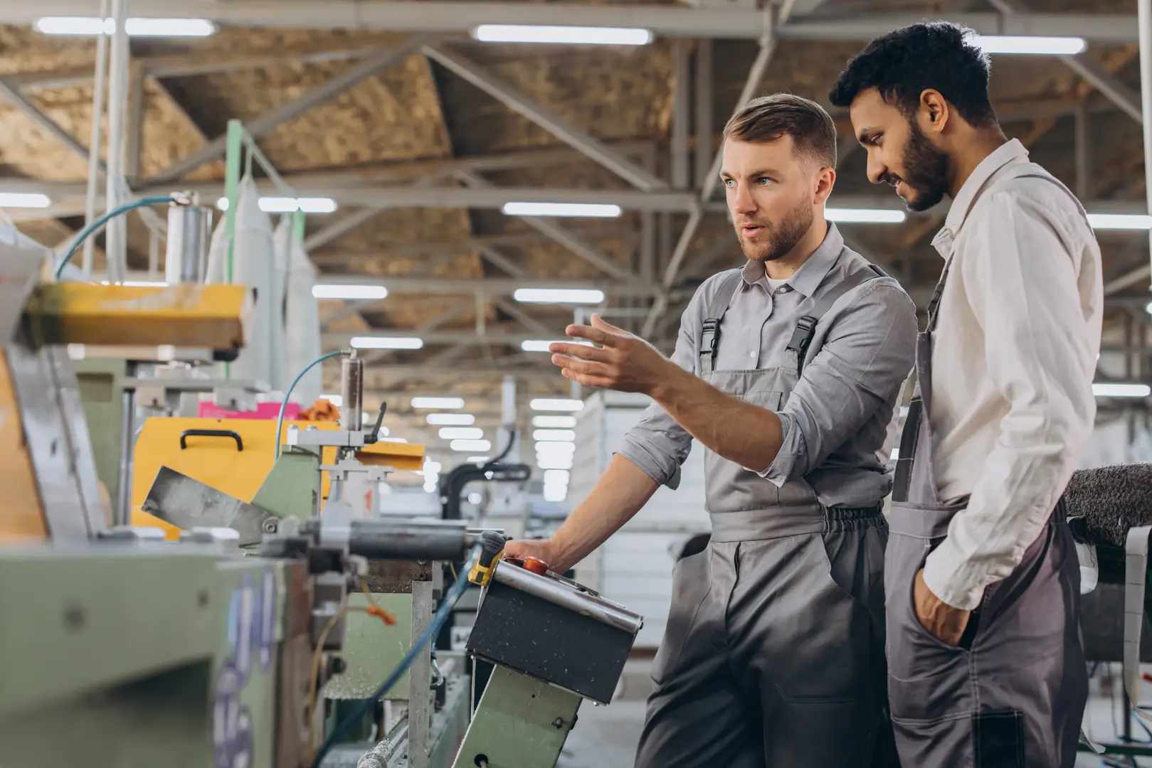 Zwei Männer in einer Kunststofffabrik. Einer im Overall erklärt dem anderen die Maschinen. Sie sind konzentriert und in ein Gespräch vertieft.