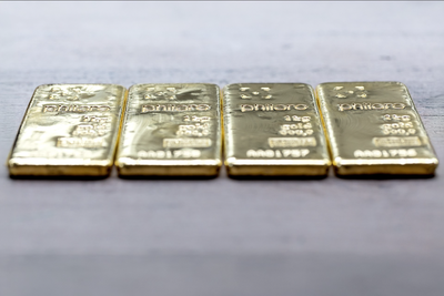 Vier Goldbarren von philoro auf grauem Untergrund aufgereiht.