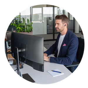 Office Arbeitswelt Ein Mann in einem Büro sitzt an einem Schreibtisch, arbeitet am Computer und trägt ein Headset. Büro im Hintergrund, Pflanzen auf dem Tisch.