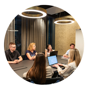 Office Arbeitswelt Sechs Personen sitzen in einem modernen Konferenzraum an einem Tisch. Sie diskutieren und verwenden Laptops. Hängeleuchten erhellen den Raum.