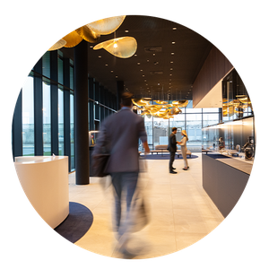 Store Arbeitswelt Moderne Büroumgebung mit unscharfer Person im Anzug, eleganten goldenen Deckenlampen und großen Fenstern mit Blick nach draußen.
