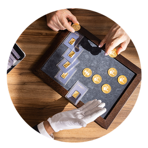 Store Arbeitswelt Hände arrangieren Goldmünzen und -barren in einem Holzkasten auf einem Tisch, neben einem Tablet. Eine Person trägt weiße Handschuhe.